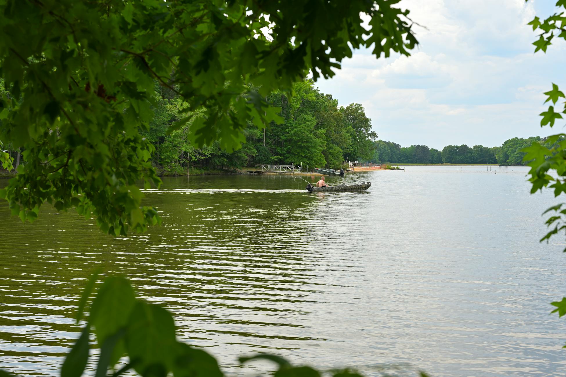 A tranquil morning scene of a fisherman on a lake surrounded by woodland.
